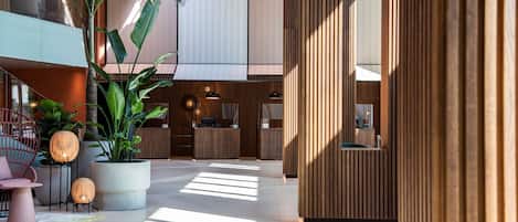 A spacious lobby with a modern design, featuring a reception desk, seating areas, and large potted plants.