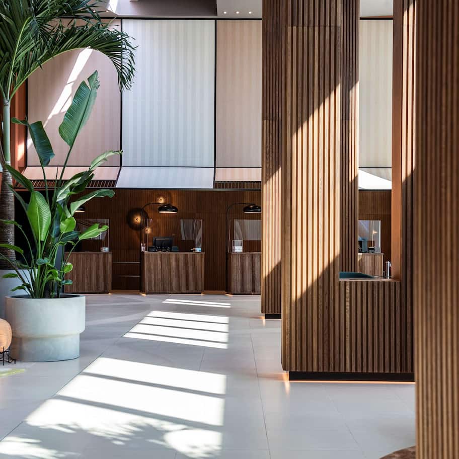 A spacious lobby with a modern design, featuring a reception desk, seating areas, and large potted plants.