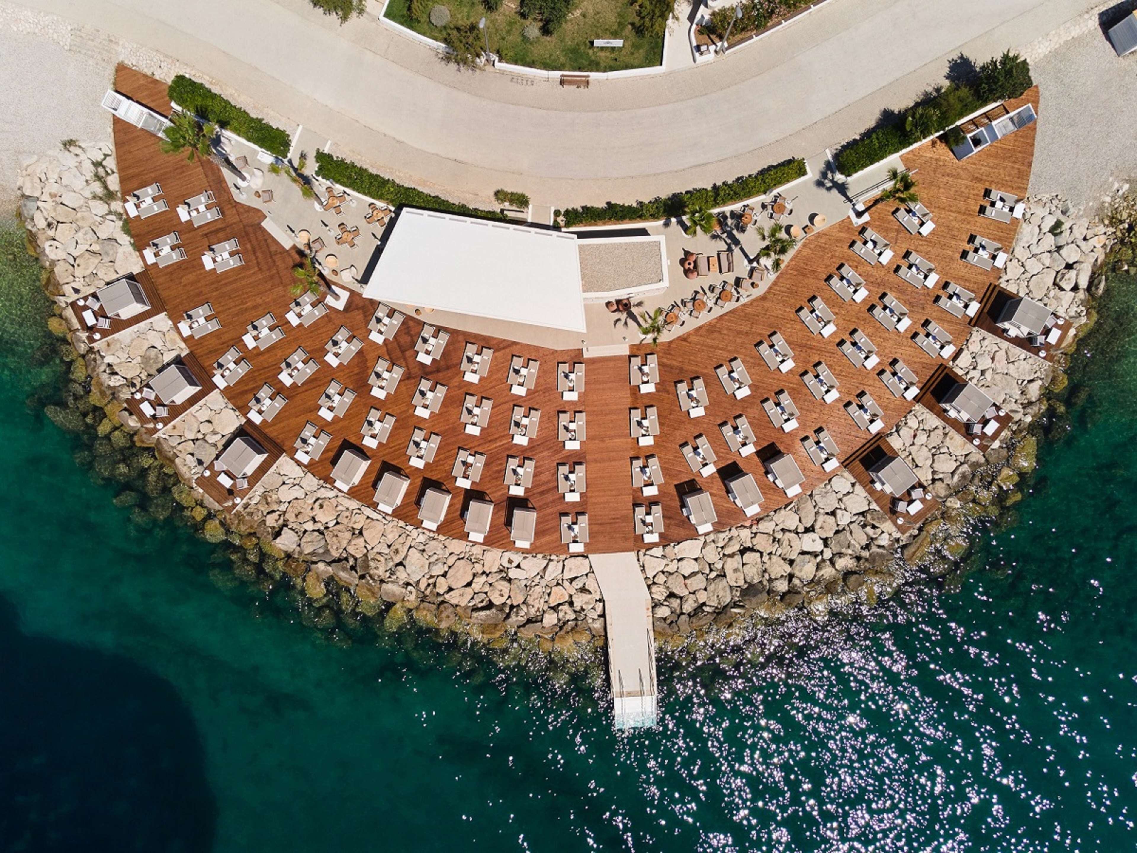An aerial view of a coastal resort with a circular layout of rooms, a central courtyard, and a rocky shoreline.