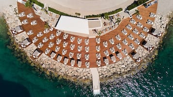 An aerial view of a coastal resort with a circular layout of rooms, a central courtyard, and a rocky shoreline.