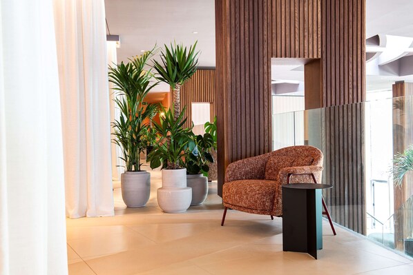 A modern lobby with a patterned armchair, large potted plants, and a glass railing.