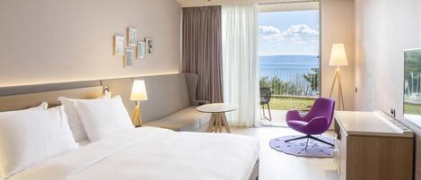 Habitación de hotel con cama, una mesita, una silla morada, un escritorio y vistas al mar.