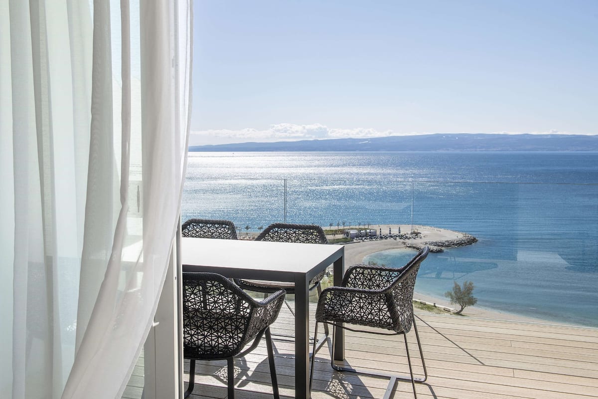 A balcony with a table and chairs overlooking a coastal view.