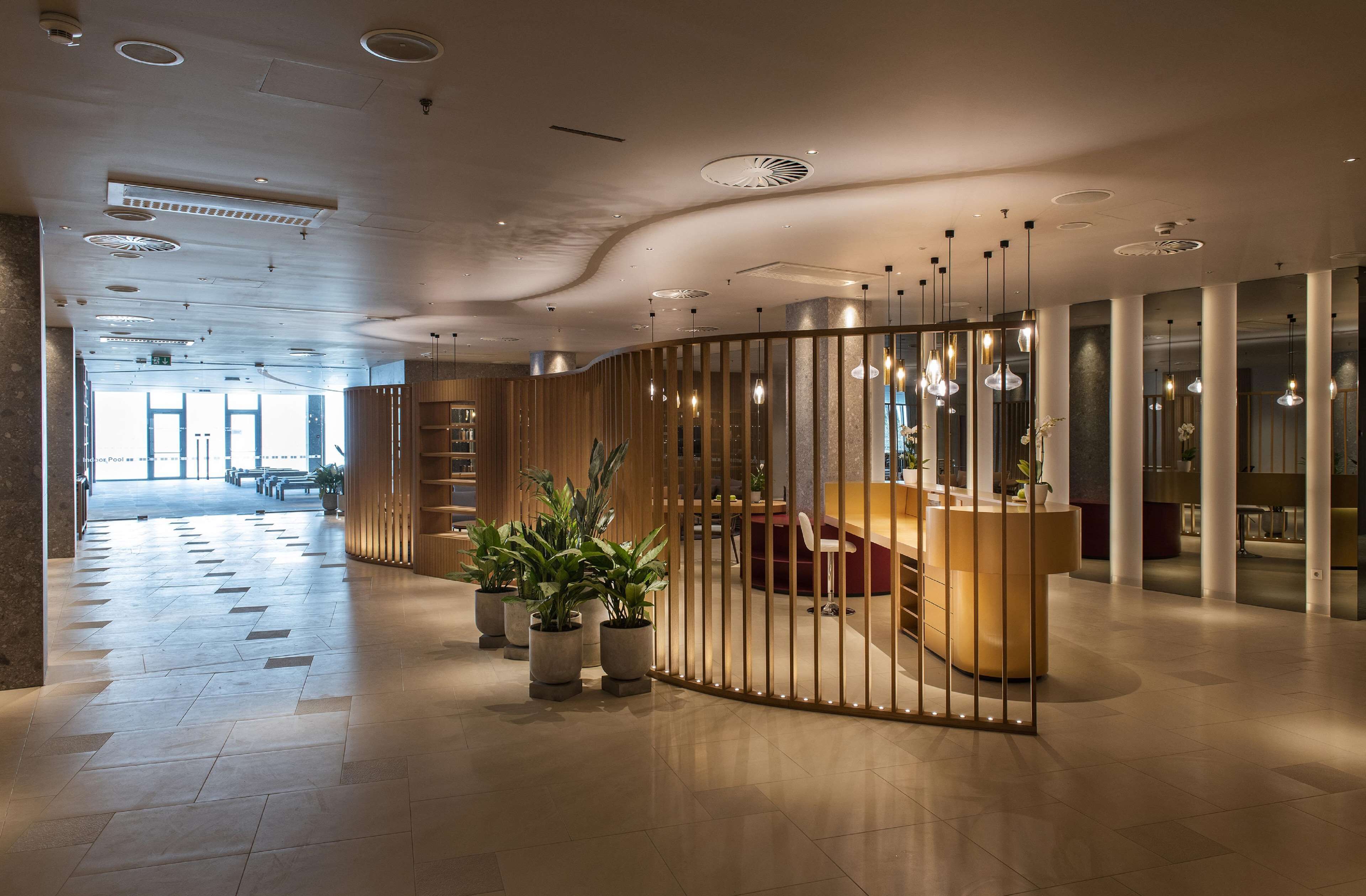 Un hall d’hôtel moderne avec un comptoir d’accueil, un espace salon et des plantes en pot.