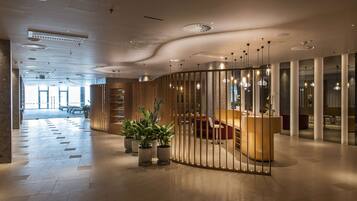 Un hall d’hôtel moderne avec un comptoir d’accueil, un espace salon et des plantes en pot.