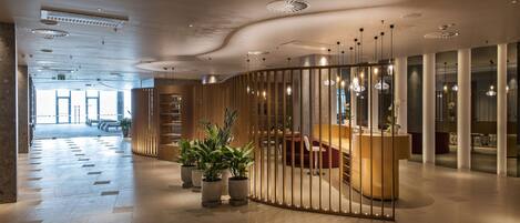 Een moderne hotellobby met een receptiebalie, een zithoek en potplanten.