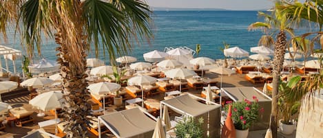 A beachside resort with multiple sun loungers and umbrellas, a pool area, and a view of the sea.