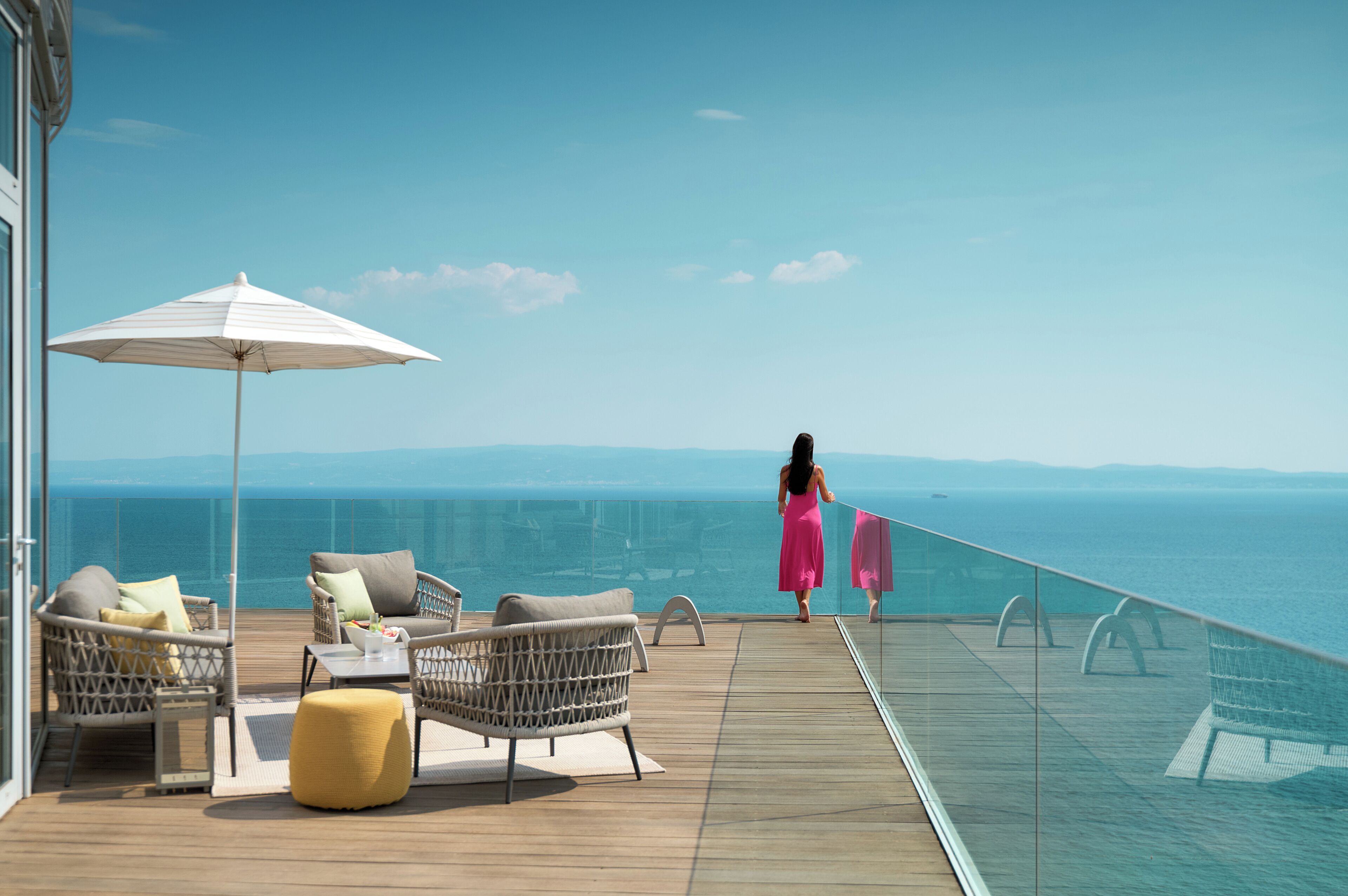Ein Balkon mit Korbmöbeln, einem weißen Sonnenschirm und Blick auf das Meer.