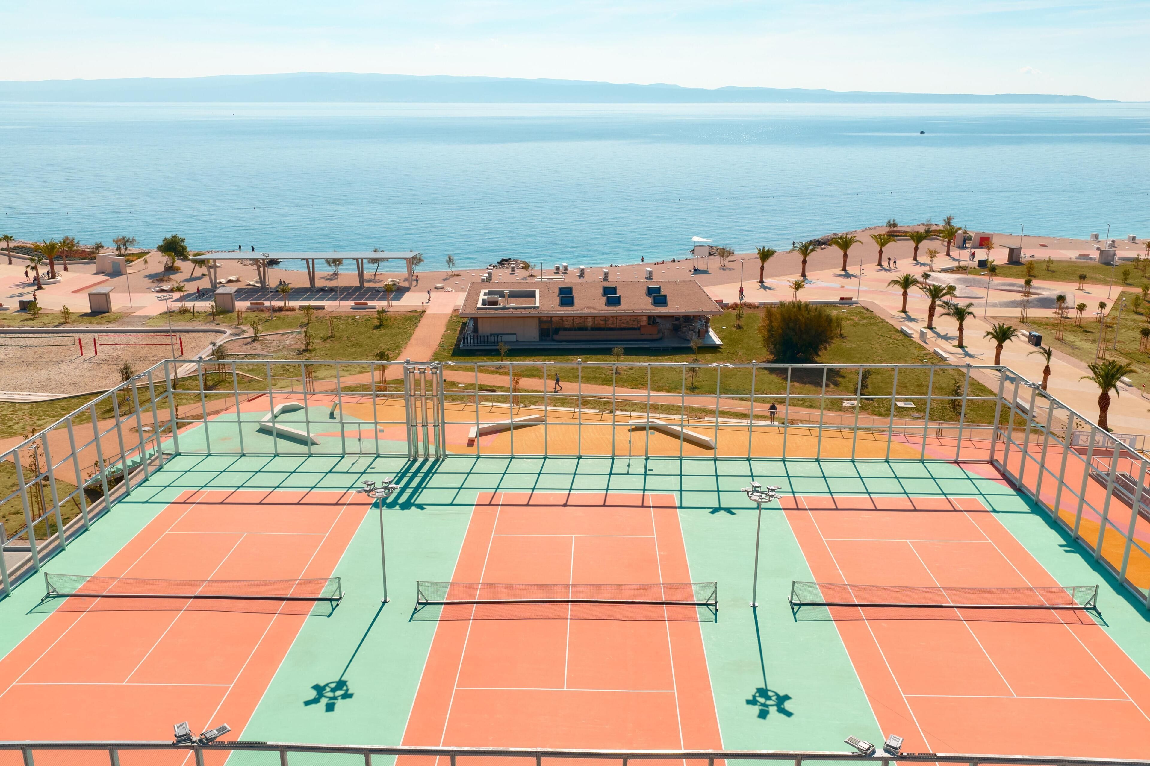 A tennis court with a view of the sea and a building in the background.