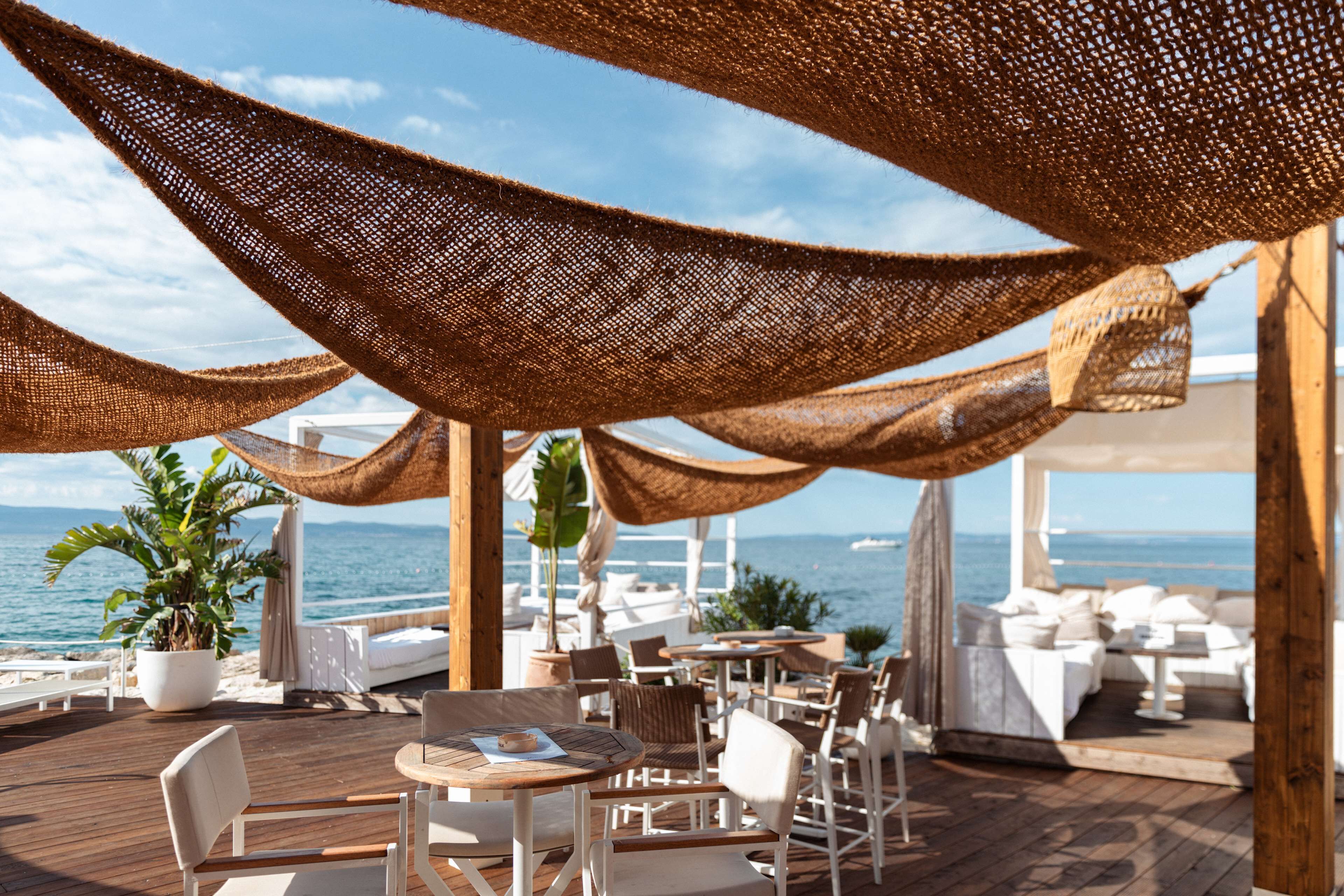 Een buitenruimte met tafels en stoelen, een houten terras en uitzicht op zee.