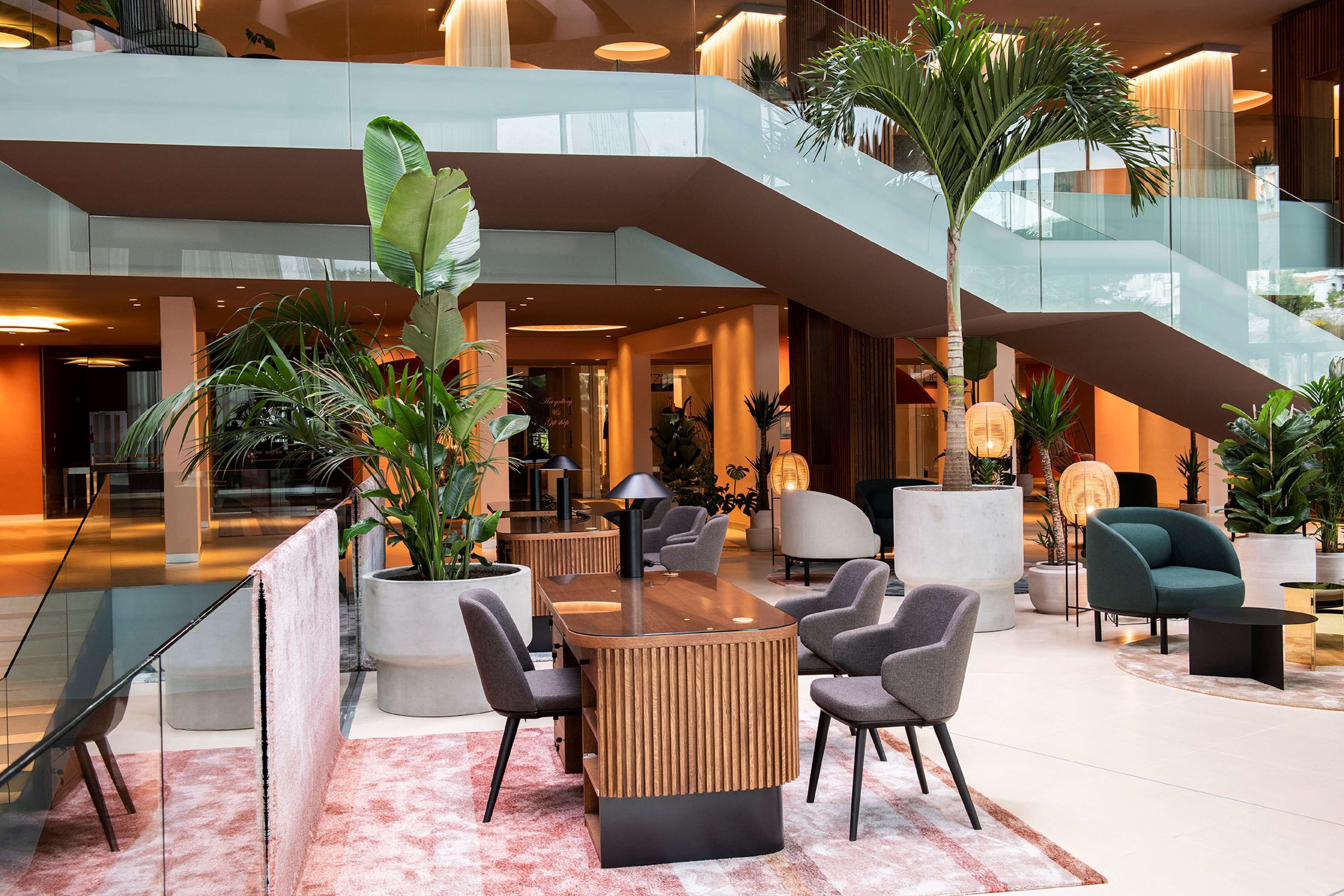 A spacious lobby with a central seating area, a staircase, and multiple potted plants.