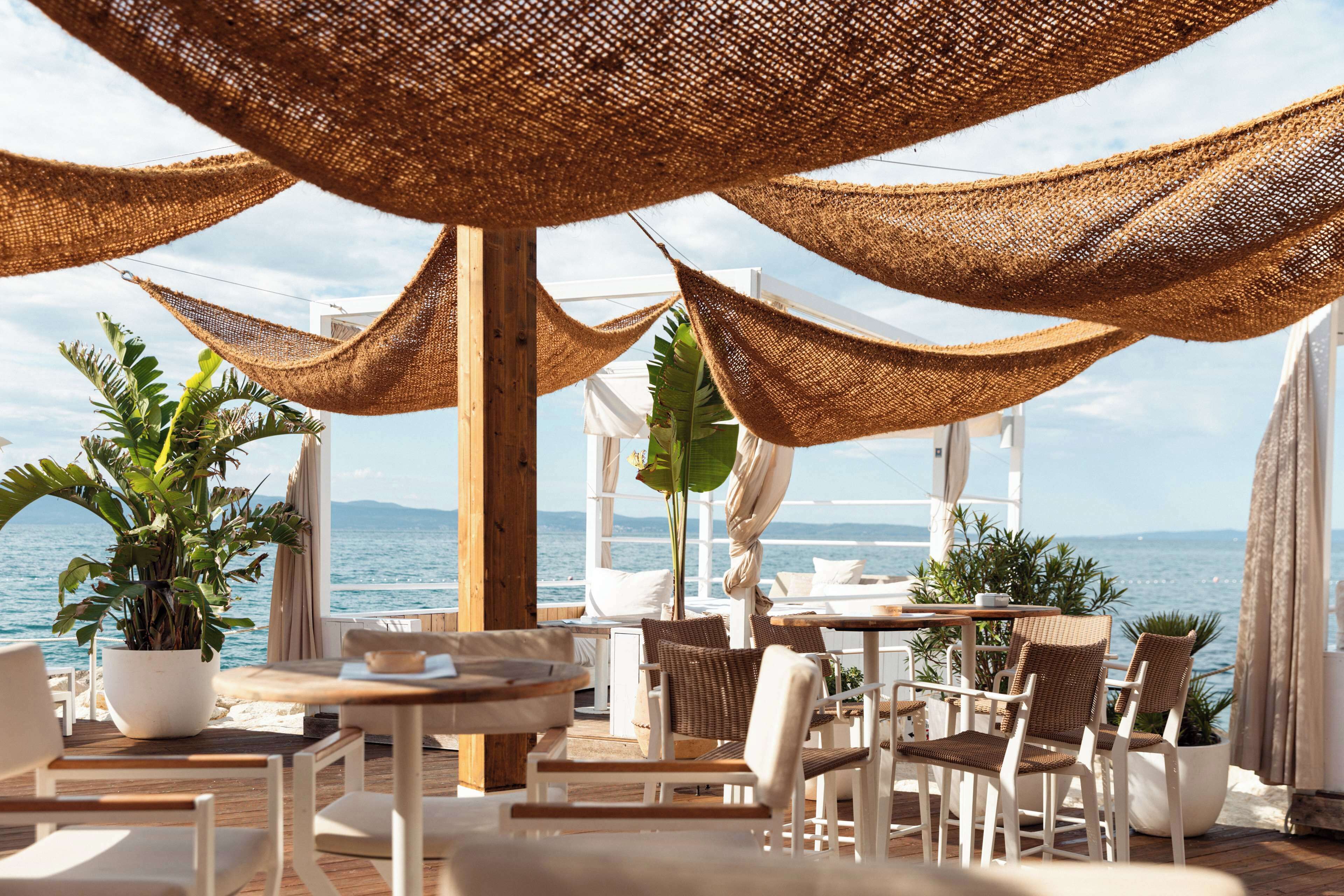 An outdoor seating area with wicker furniture and potted plants, overlooking a body of water.
