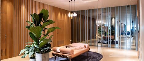 A modern lobby with a lounge area featuring a sofa, potted plants, and a glass partition.