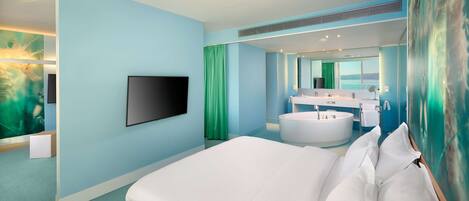 A modern hotel room with a large bed, a flat-screen TV, a bathtub, and a bathroom with a sink and mirror.