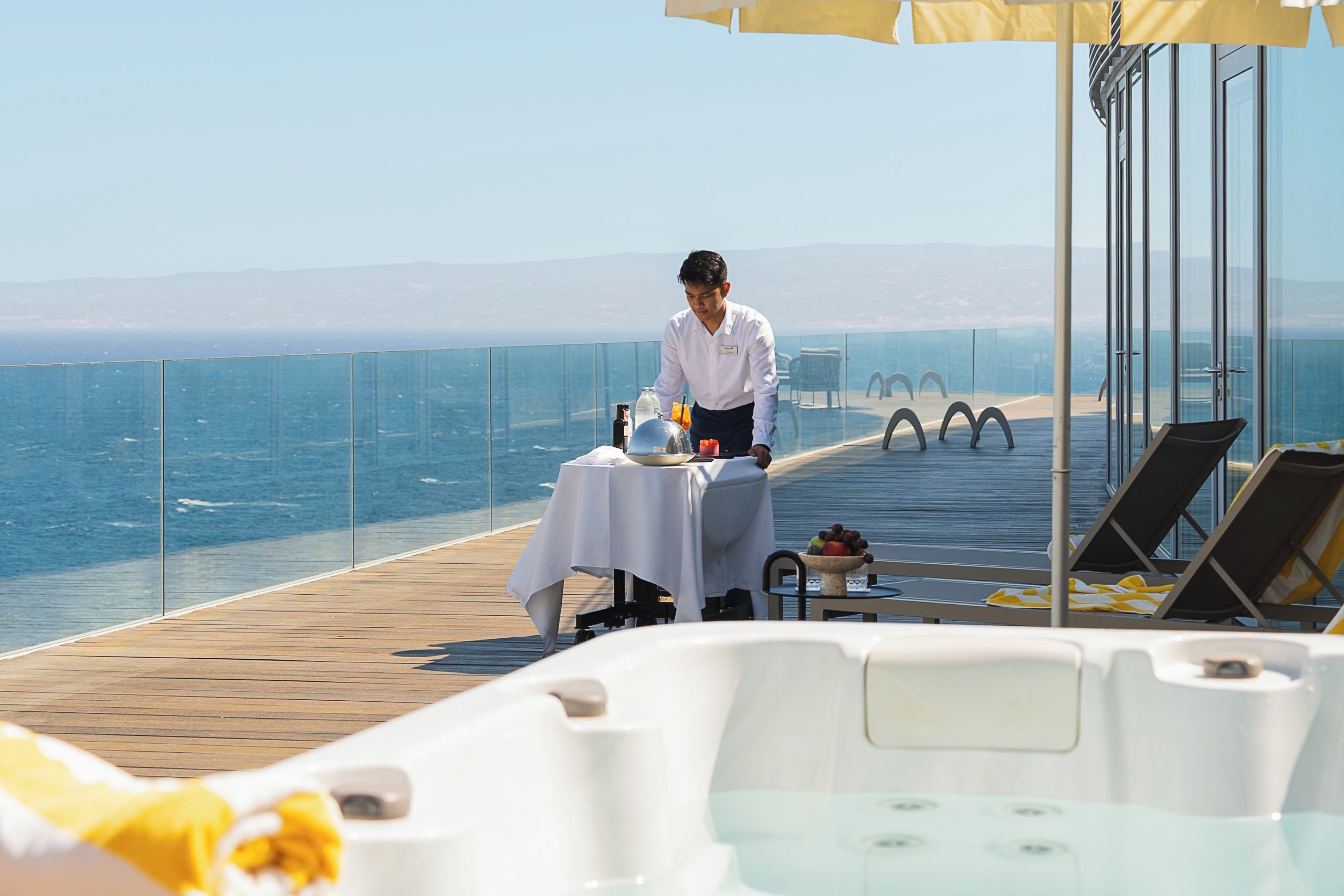 A person setting up a table on a deck with a view of the sea.