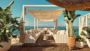 A beachside lounge with white furniture, a pergola, and potted plants.
