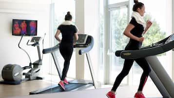 Academia com esteiras, espelho e televisão exibindo vídeos de exercícios.