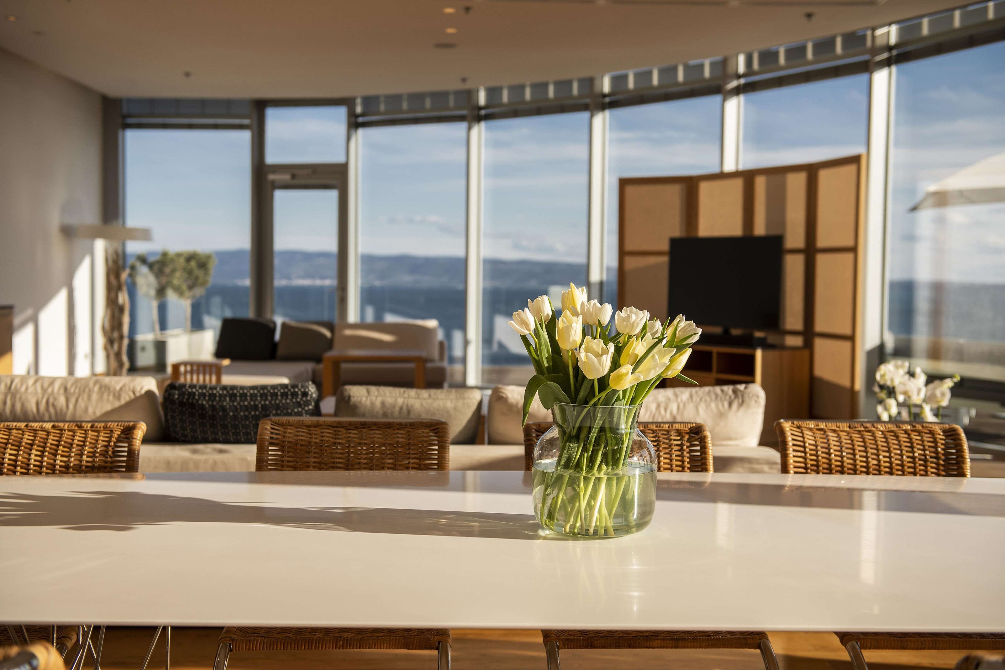 A modern living room with a large window, a white table, and a vase of white flowers.