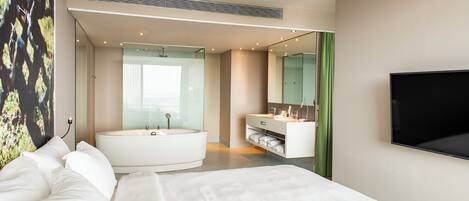 A modern hotel room with a large bed, a separate bathroom with a bathtub, a flat-screen TV, and a large window.