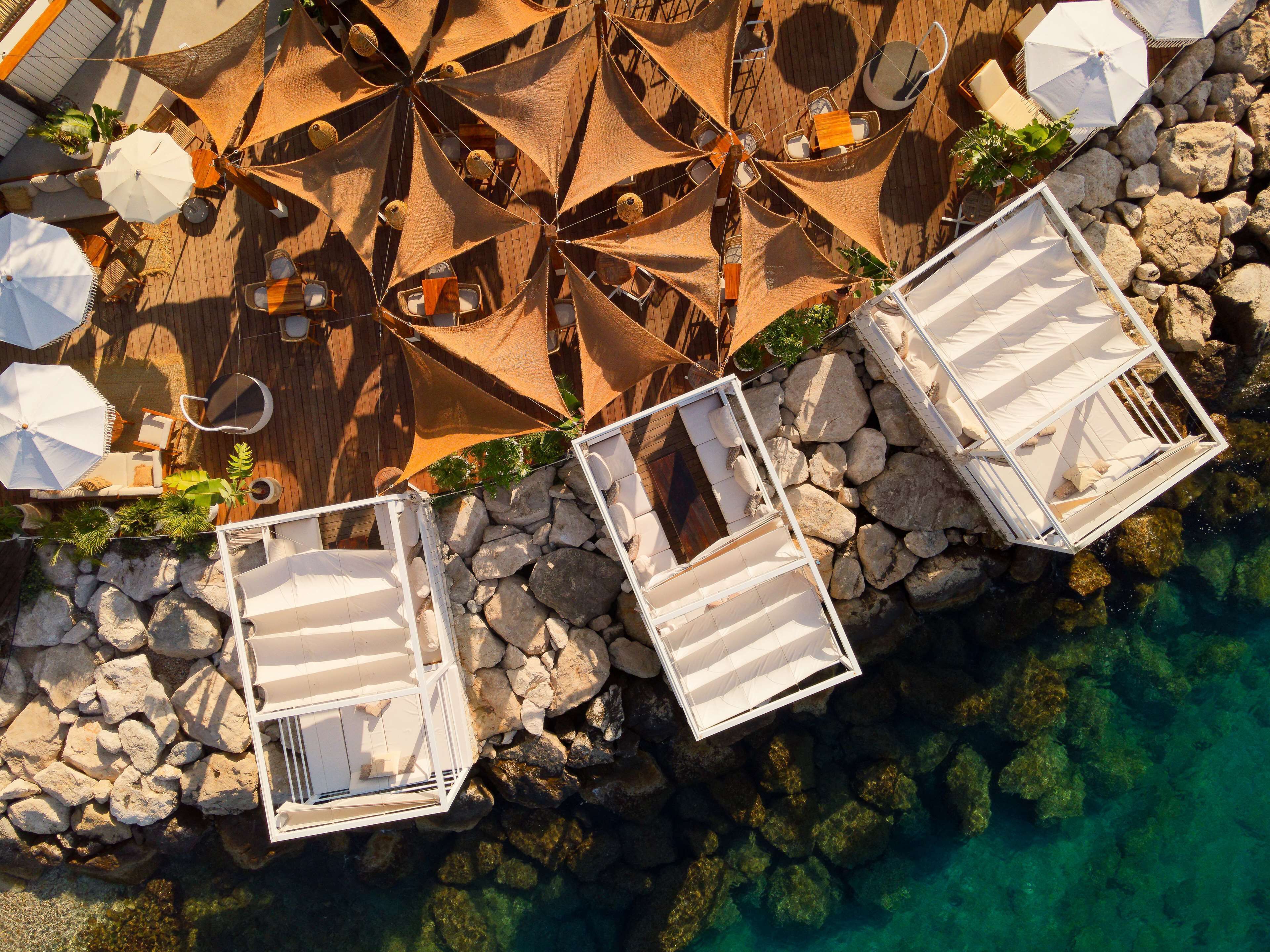 Vue aérienne d’un complexe hôtelier doté d’espaces de détente en plein air, de chaises longues blanches et d’une côte rocheuse.
