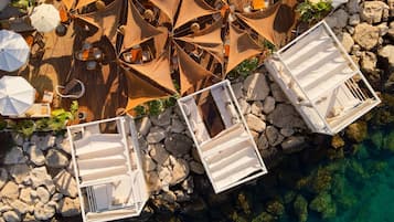 Vue aérienne d’un complexe hôtelier doté d’espaces de détente en plein air, de chaises longues blanches et d’une côte rocheuse.