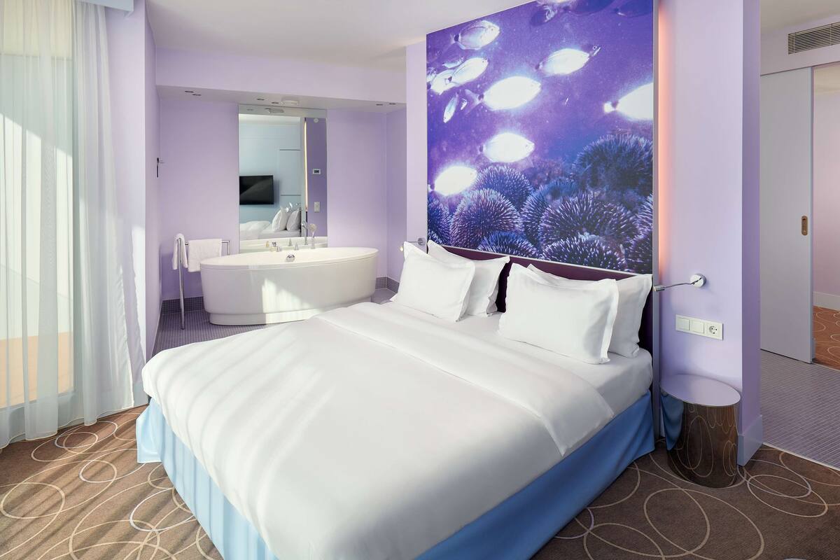 A modern hotel room with a large bed, a separate bathroom with a bathtub, and a large wall mural of fish.