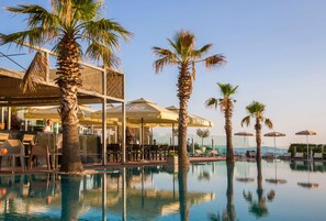 A pool area with palm trees, lounge chairs, and umbrellas.
