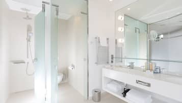 A modern bathroom with a glass shower enclosure, a large mirror with lights, and a white vanity with a towel rack.
