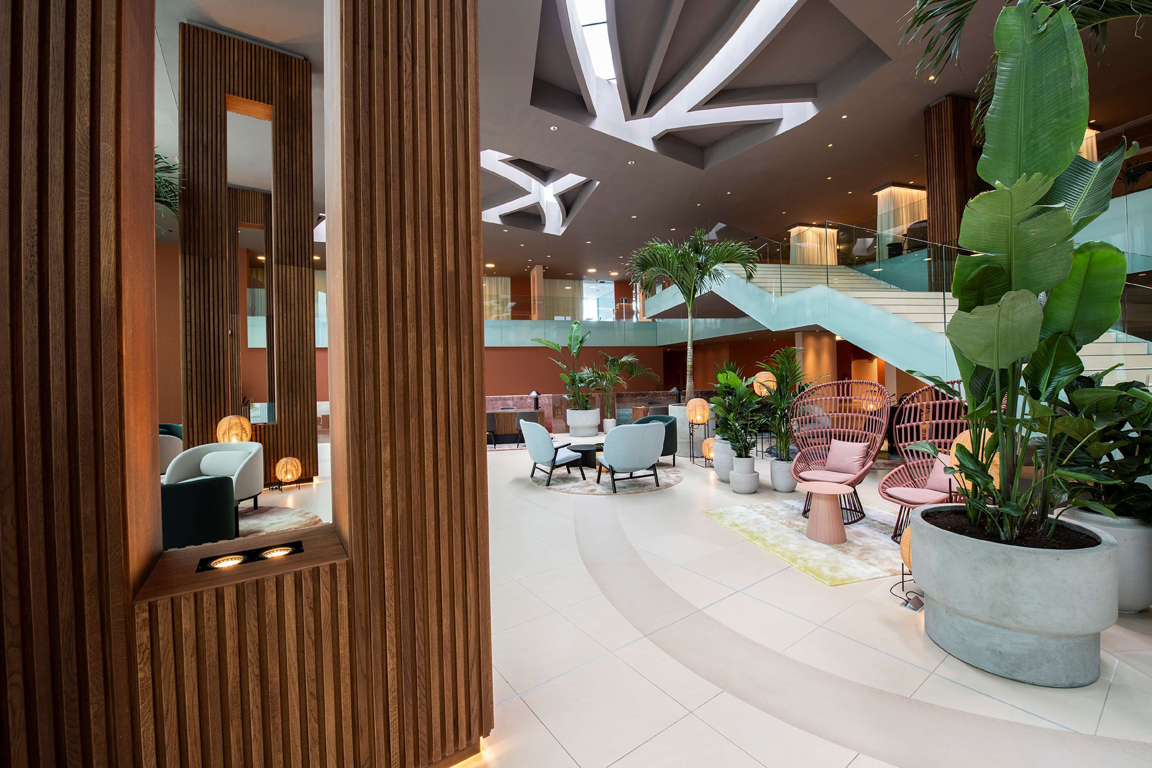 A modern indoor space with a central seating area, a staircase, and a large potted plant.