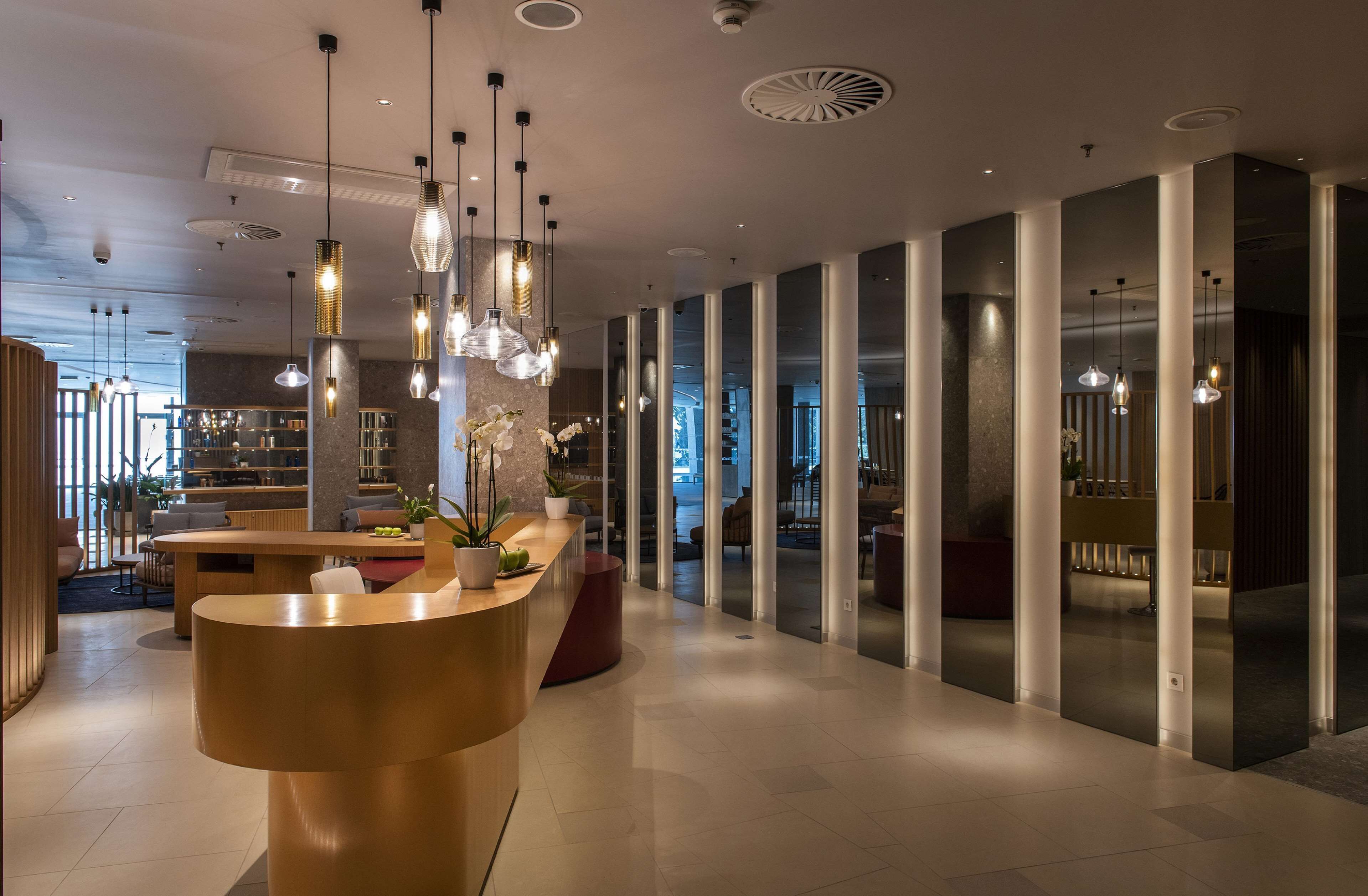Un hall d’hôtel moderne avec un comptoir d’accueil, des luminaires suspendus et une vue sur le bar.