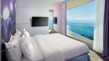 A hotel room with a large bed, a flat-screen TV, and a balcony with a view of the sea.