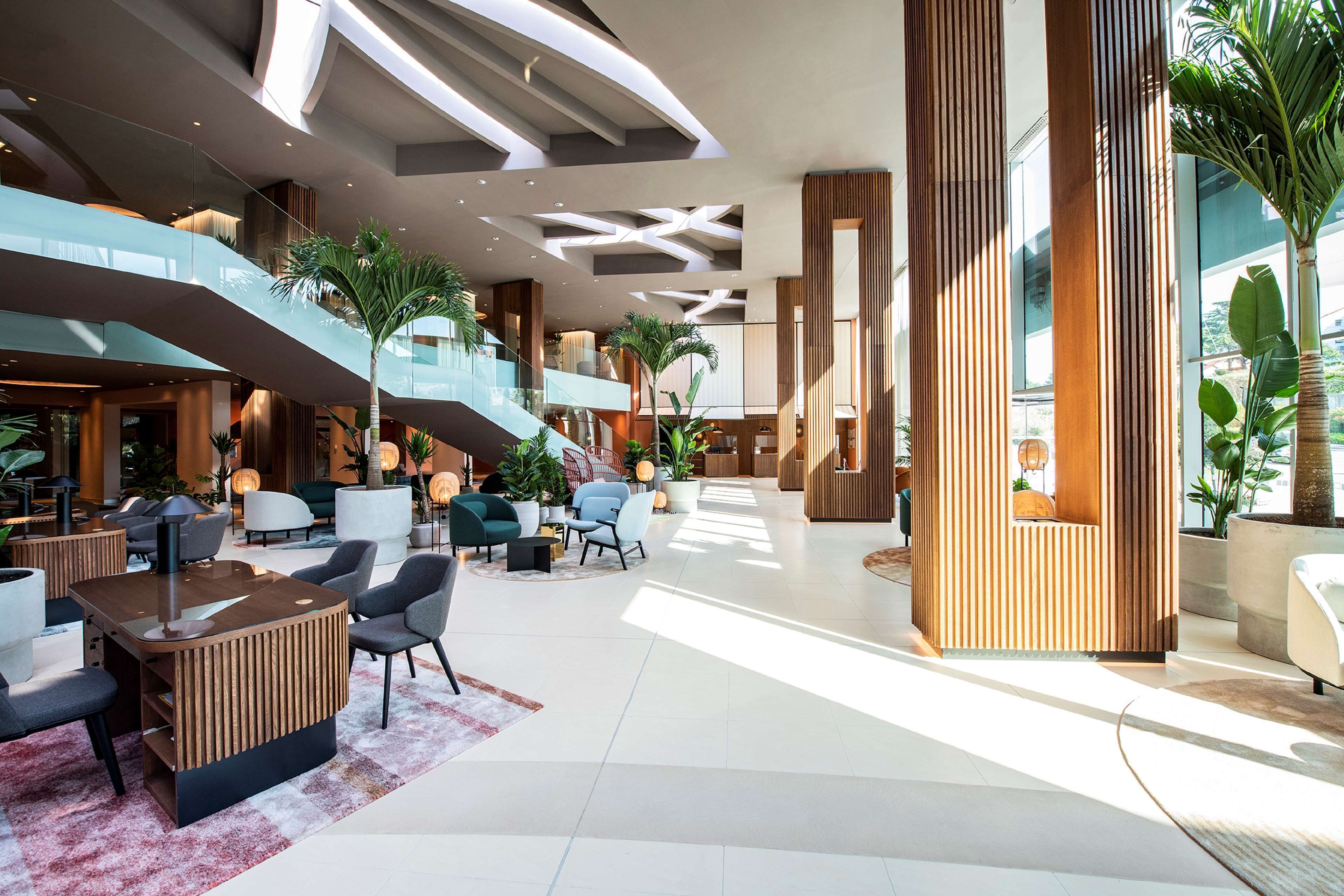 A spacious lobby with a central seating area, a staircase, and large windows allowing natural light.