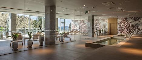 Un vestíbulo moderno con paredes de vidrio, zona de piscina y sillones de descanso.