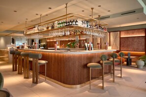 A bar area with a wooden counter, multiple bar stools, and a variety of bottles and glasses.
