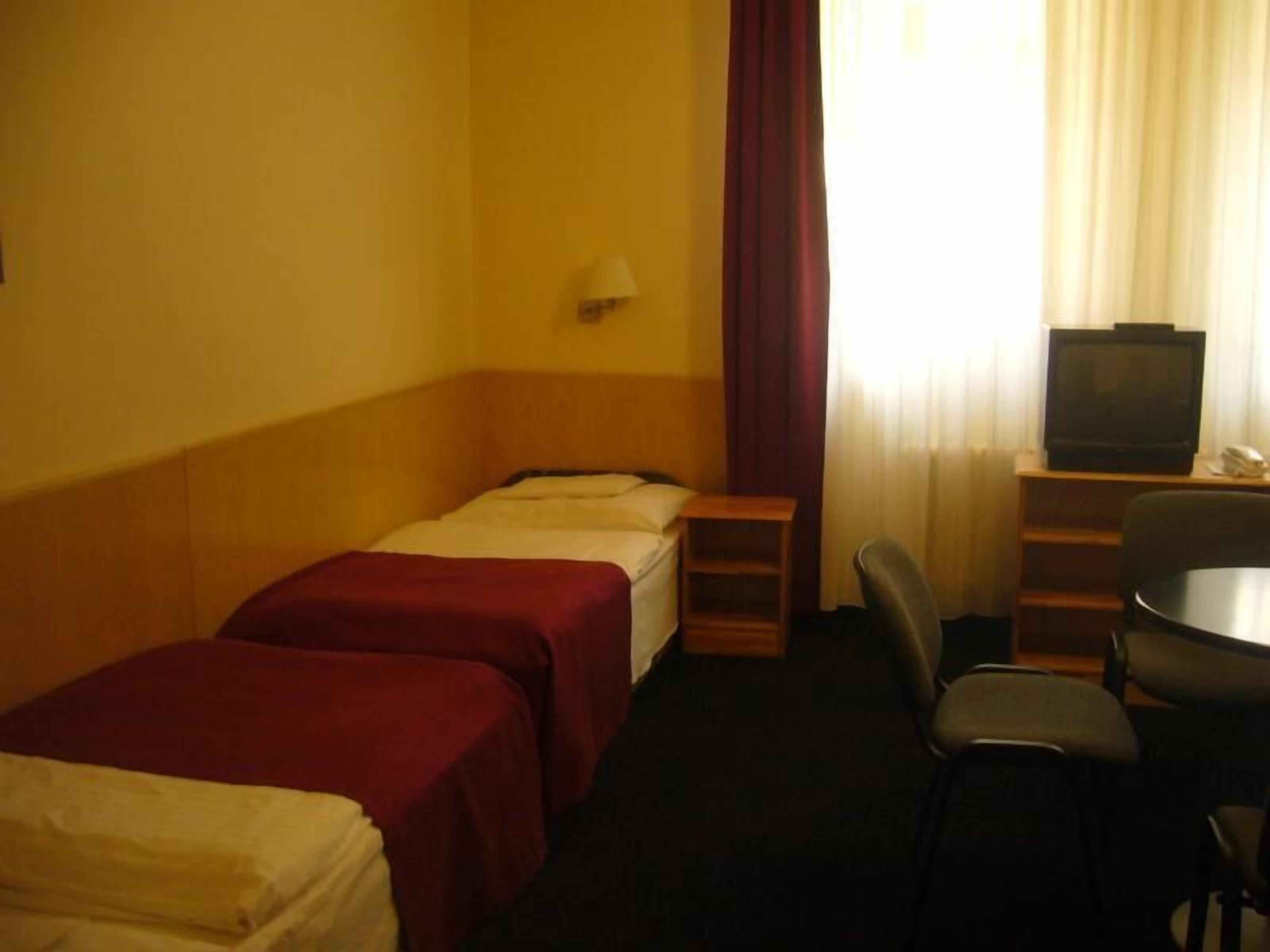 Une chambre d’hôtel avec deux lits simples, un bureau avec une chaise, une télévision et une fenêtre avec des rideaux.