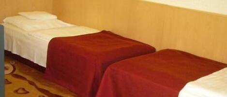 A hotel room with two single beds, a wooden floor, and a framed picture on the wall.