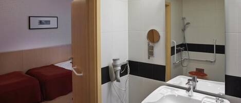 A bathroom with a white sink, a mirror, and a shower. There are two red stools and a framed picture on the wall.