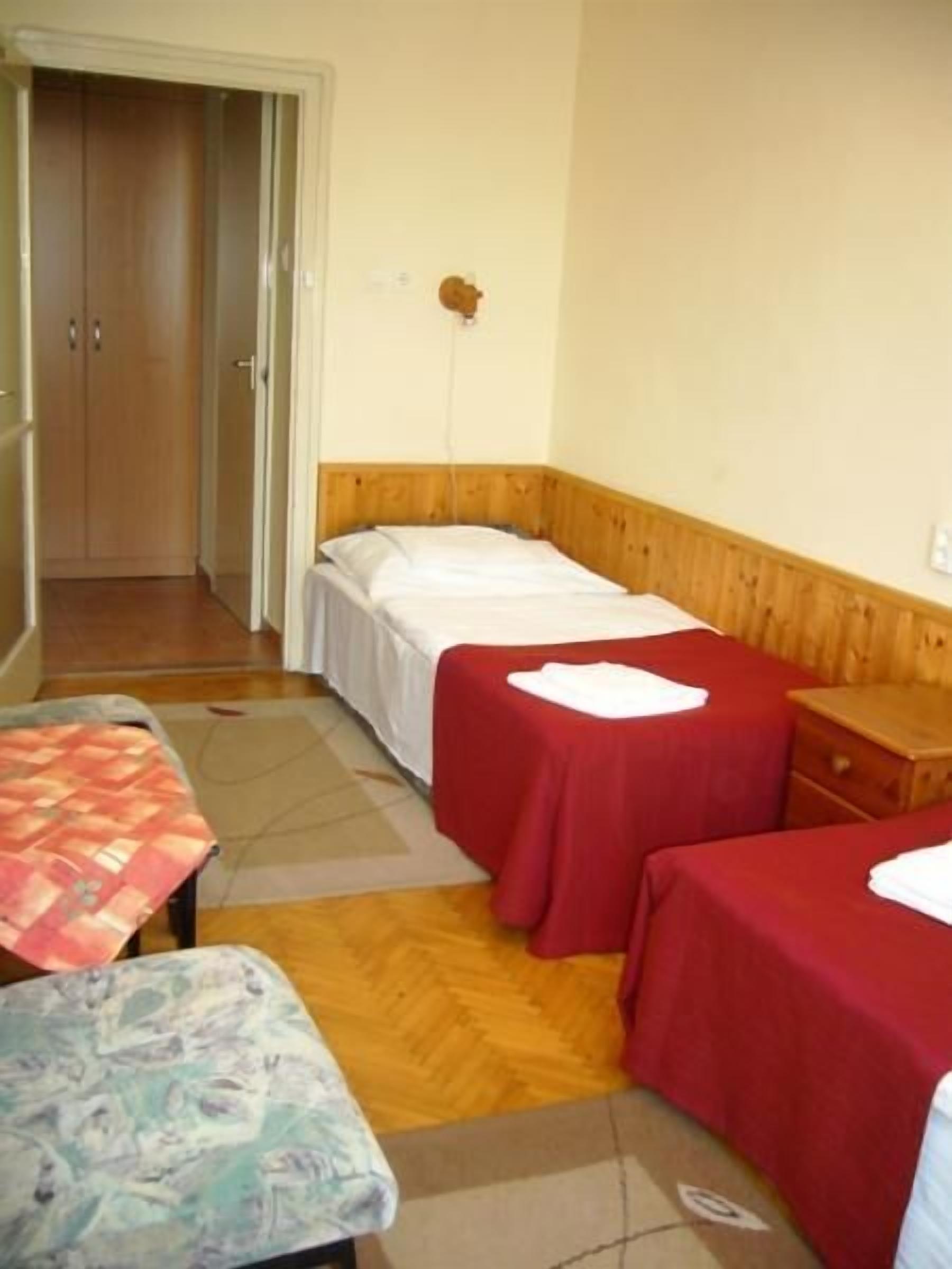 Een kamer met twee bedden, een houten hoofdbord, een tafeltje en een bankje.