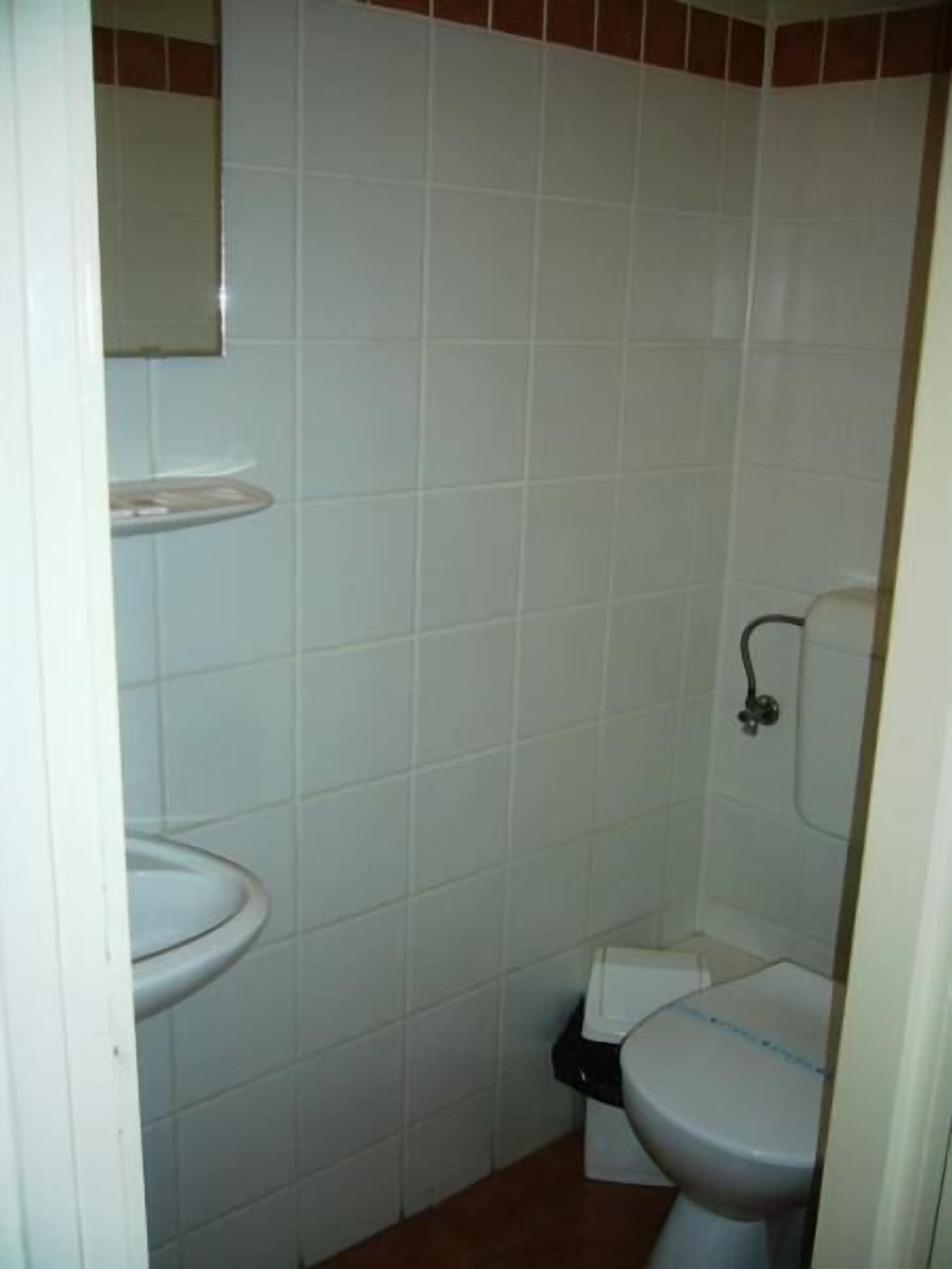 A small, tiled bathroom with a toilet, a sink, and a mirror above the sink.