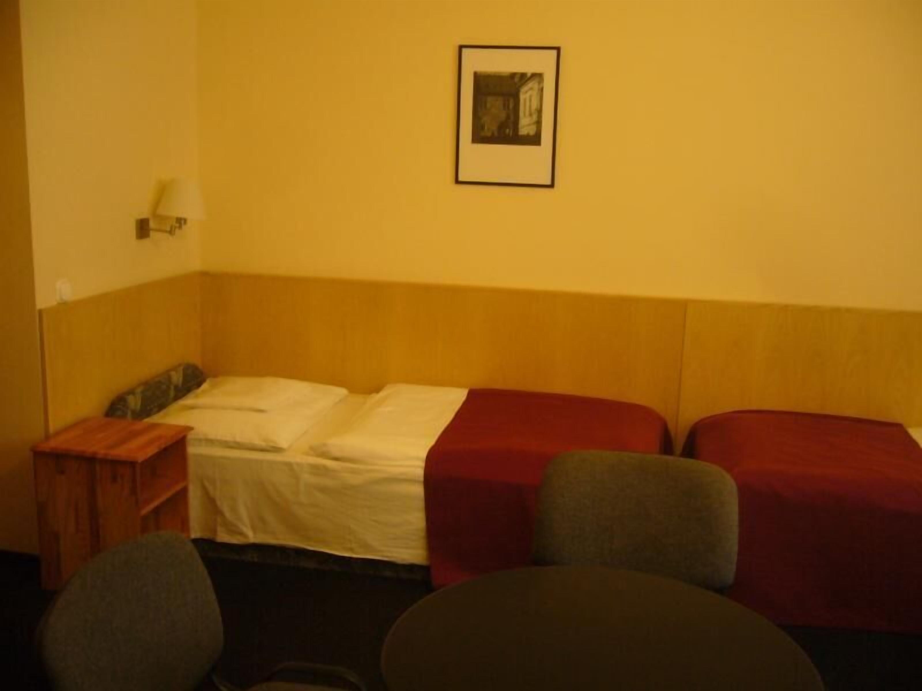 Ein Hotelzimmer mit einem Einzelbett, einem Nachttisch, einer Lampe und einem gerahmten Bild an der Wand.