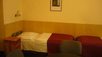 Ein Hotelzimmer mit einem Einzelbett, einem Nachttisch, einer Lampe und einem gerahmten Bild an der Wand.
