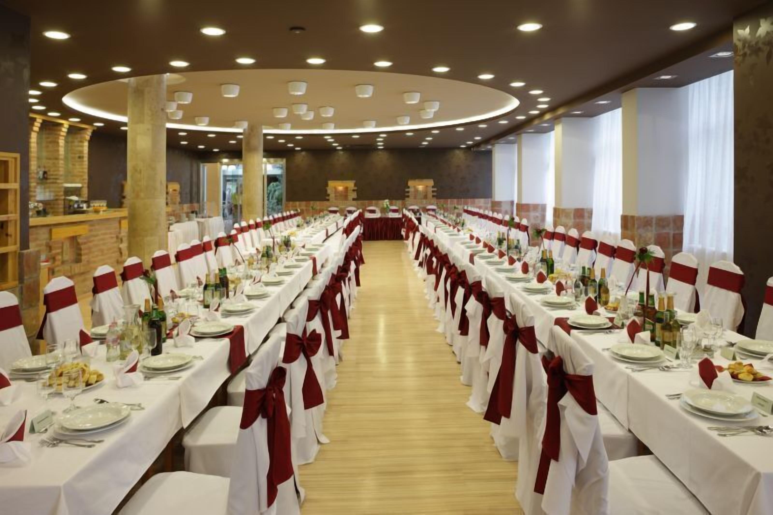 A banquet hall with long tables set for a formal event, featuring white tablecloths and red sashes.