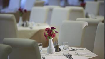 Une table à manger dressée avec un vase blanc rempli de fleurs, des verres à eau et des couverts.