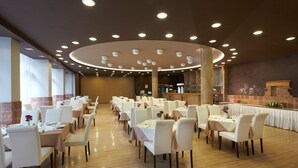A spacious dining area with multiple tables and chairs, a brick wall, and a stone fireplace. - Hotel Laterum (Pecs)