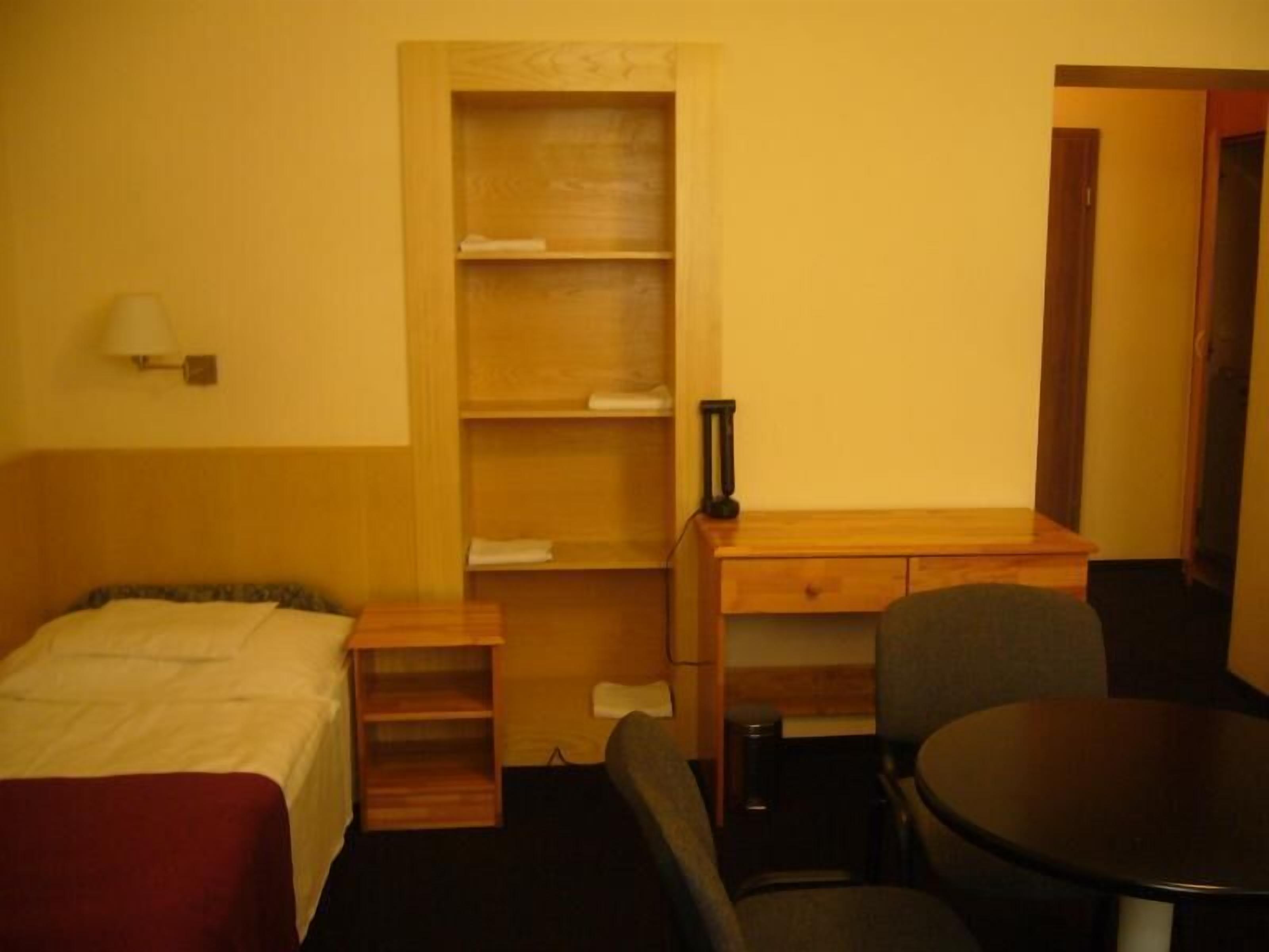Une chambre d’hôtel de taille réduite, comprenant un lit simple, un petit bureau, une chaise et une table.