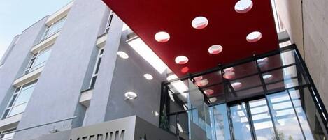 Een moderne hotelentree met een opvallende rode luifel en een bord waarop 'HOTELLATERUM' staat.