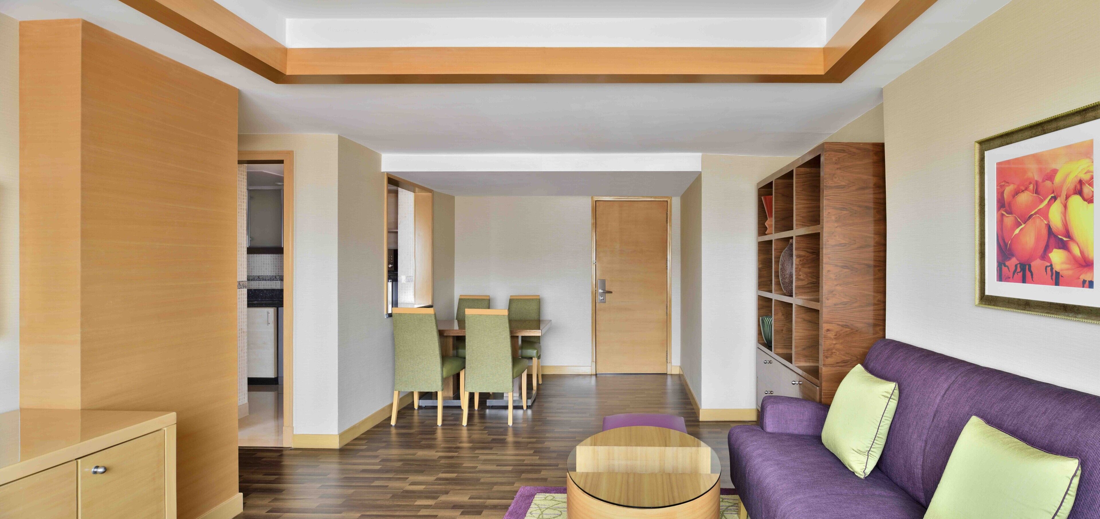 A modern living room with a purple sofa, a wooden coffee table, and a dining area with green chairs.