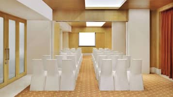 Un salón de conferencias con filas de sillas blancas, una alfombra estampada y un amplio ventanal al frente.