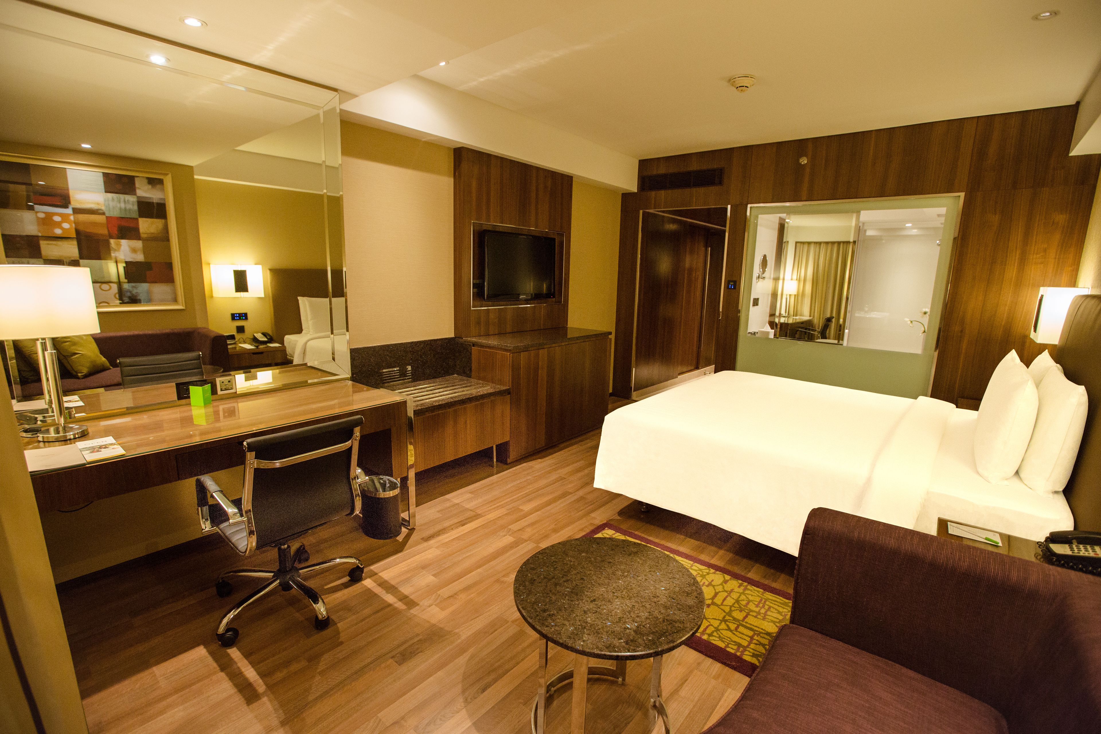 A hotel room with a bed, a desk, a chair, a TV, and a mirror.