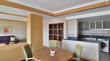 Una cocina moderna con electrodomésticos integrados, una zona de comedor con una mesa redonda y sillas, y una sala de estar con sofá y obras de arte.